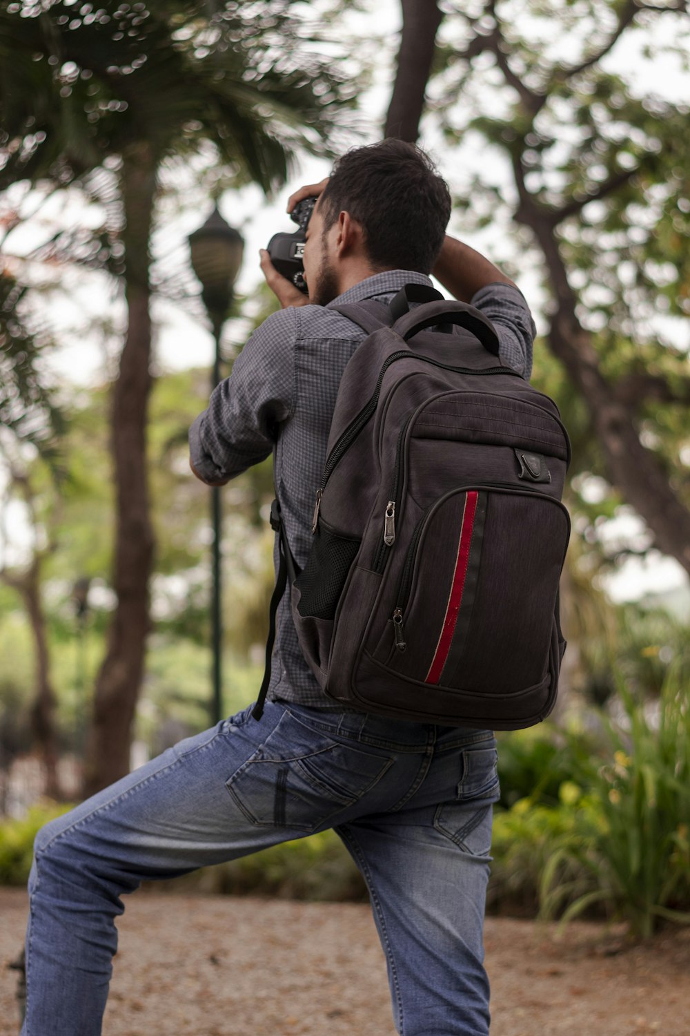 man wearing gray long-sleeved shirt with black backpack standing while taking photo on trees during daytime
