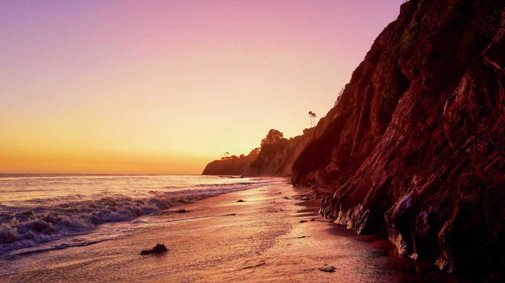 landscape photography of cliff viewing body of water under orange sky