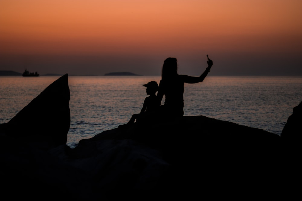 woman and boy sitting on rock on shore during golden hour