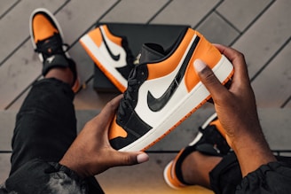 person sitting and holding orange-white-and-black Nike SB low-top sneaker