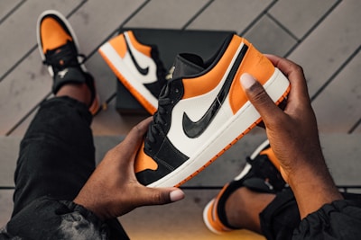 person sitting and holding orange-white-and-black Nike SB low-top sneaker