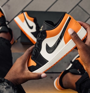 person sitting and holding orange-white-and-black Nike SB low-top sneaker