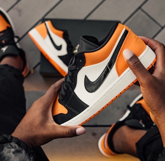 person sitting and holding orange-white-and-black Nike SB low-top sneaker