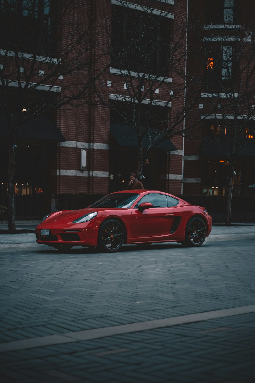 red coupe parking near road beside brown high-rise buildings