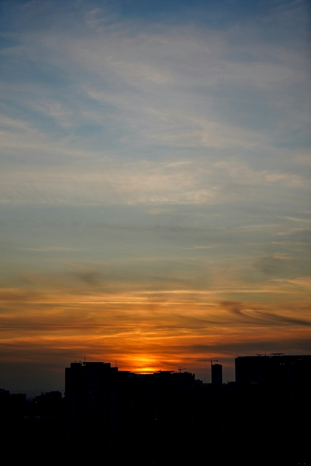 silhouette of buildings under blue, orange, and white sky