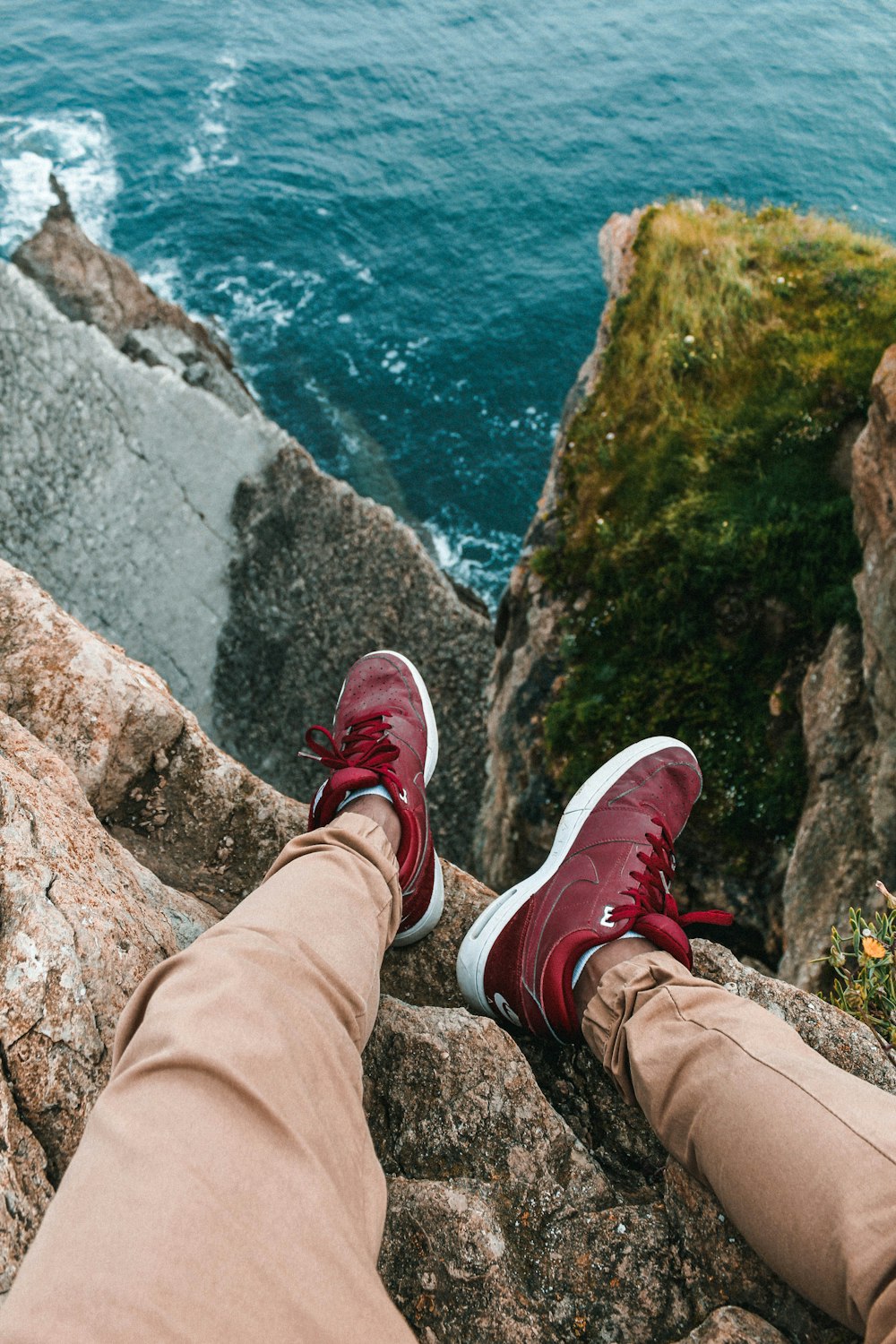 a person with red shoes is sitting on a rock by the ocean