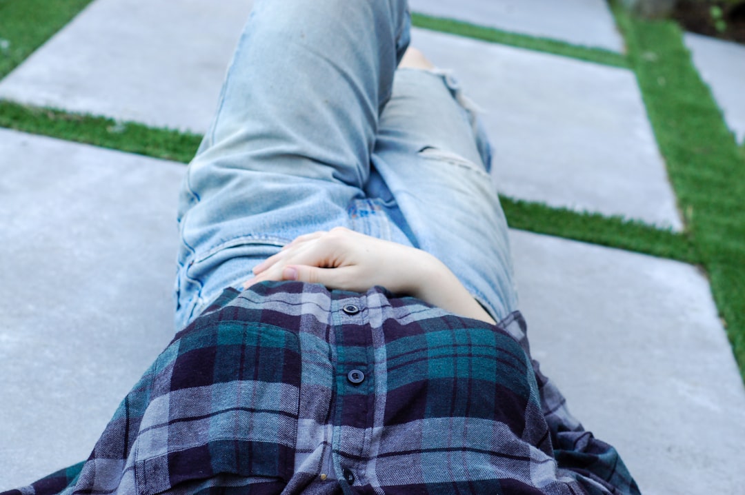 person wearing distressed blue denim bottoms and blue, purple, and black plaid button-up shirt lying on concrete pavement