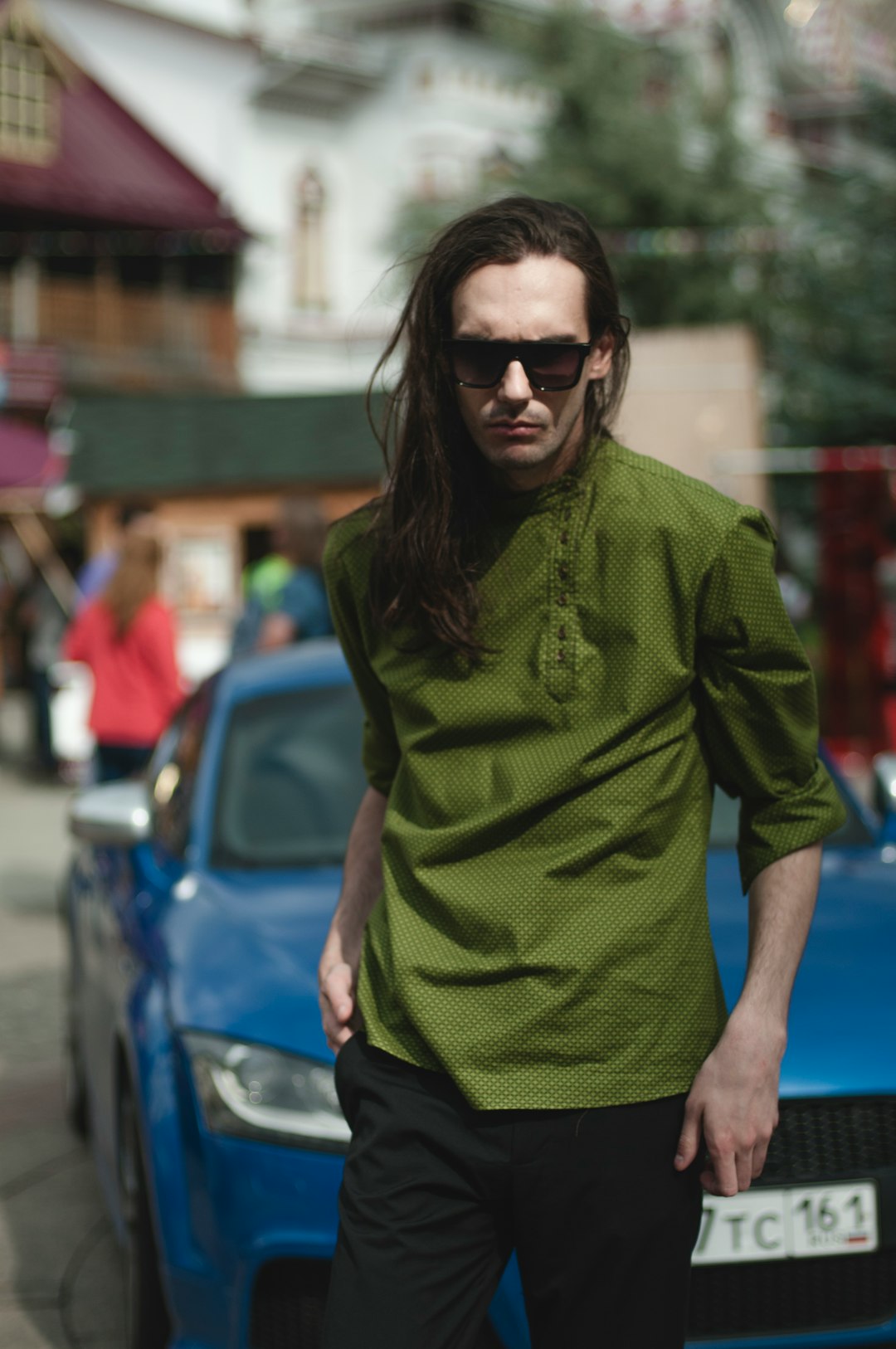 man wearing sunglasses standing in front of blue car during daytime