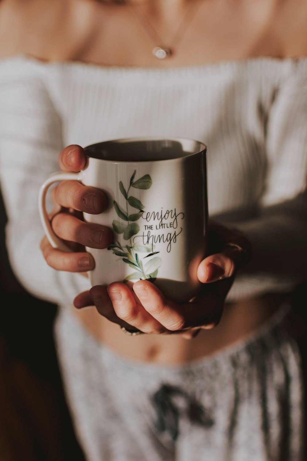 woman holding white and green floral ceramic mug while standing