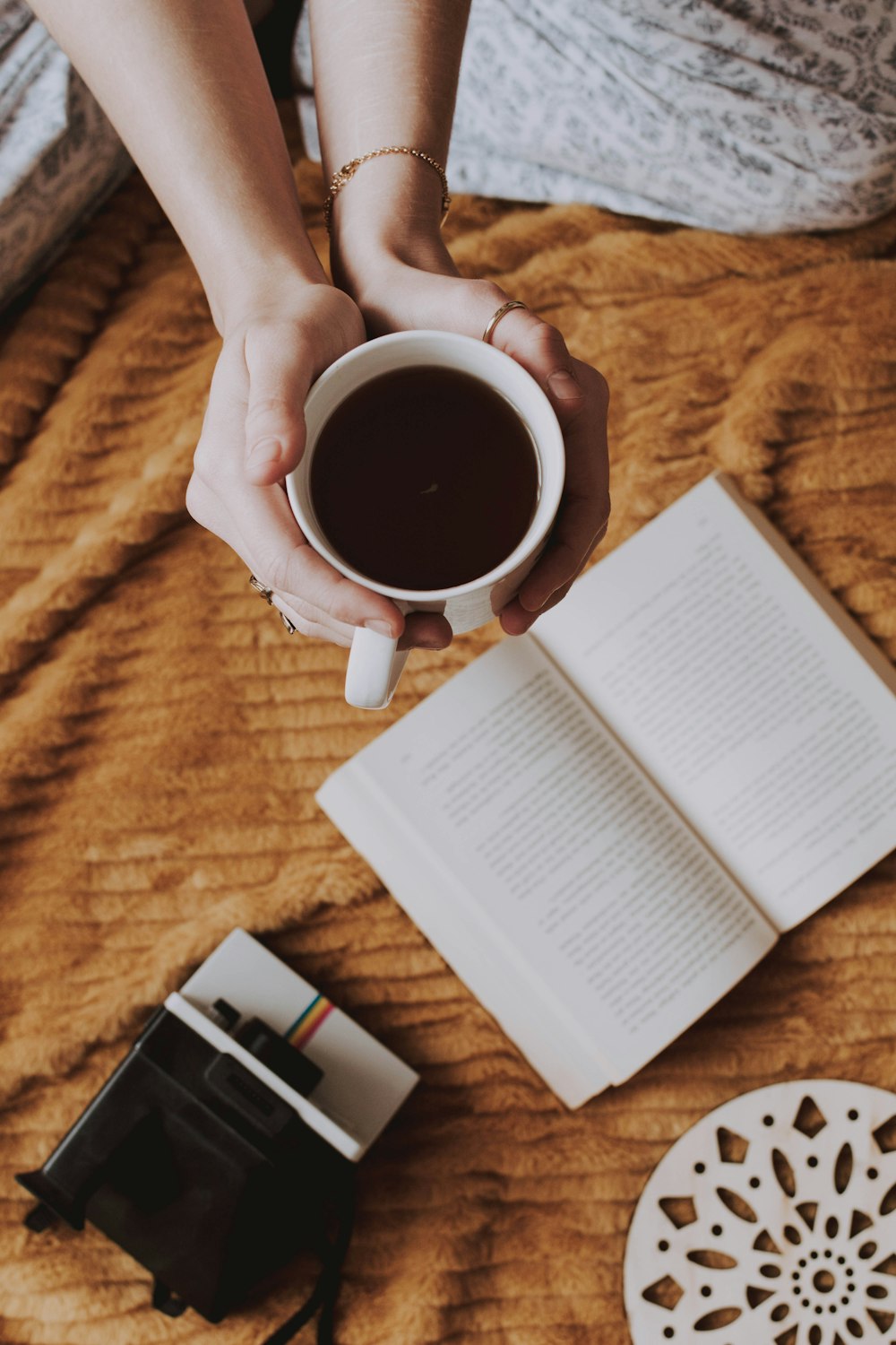 schwarzer Kaffee in weißem Keramikbecher in der Nähe eines aufgeschlagenen Buches und einer schwarz-weißen Polaroid-Kamera