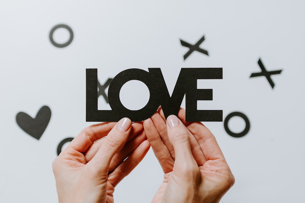 person holding black love cutout paper