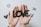 Two hands hold a cut-out word 'LOVE' in black letters. The background features scattered black paper shapes such as hearts, circles, and Xs on a light surface.