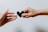 Two hands reaching towards each other, one holding a small black heart-shaped object, symbolizing connection or offering.