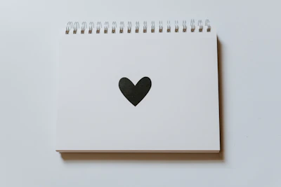 A white notebook adorned with a black line drawing of a third eye surrounded by subtle geometric shapes.