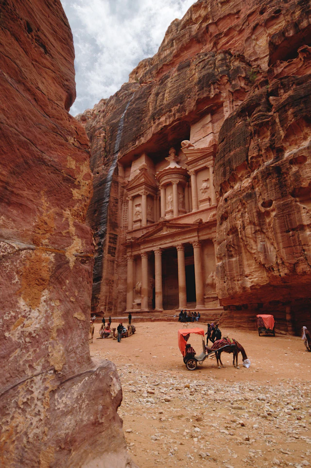 The Treasury's carved facade seen through the narrow red-rock Siq, with a horse and carriage waiting in front