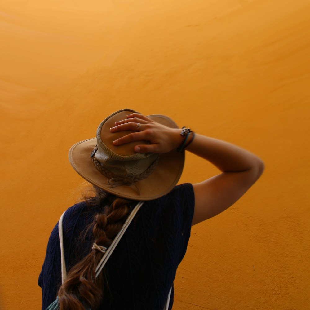 a woman wearing a hat standing in front of a yellow wall