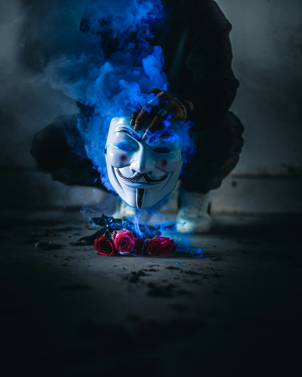 personne tenant le masque de Guy Fawkes au-dessus de roses rouges fumantes