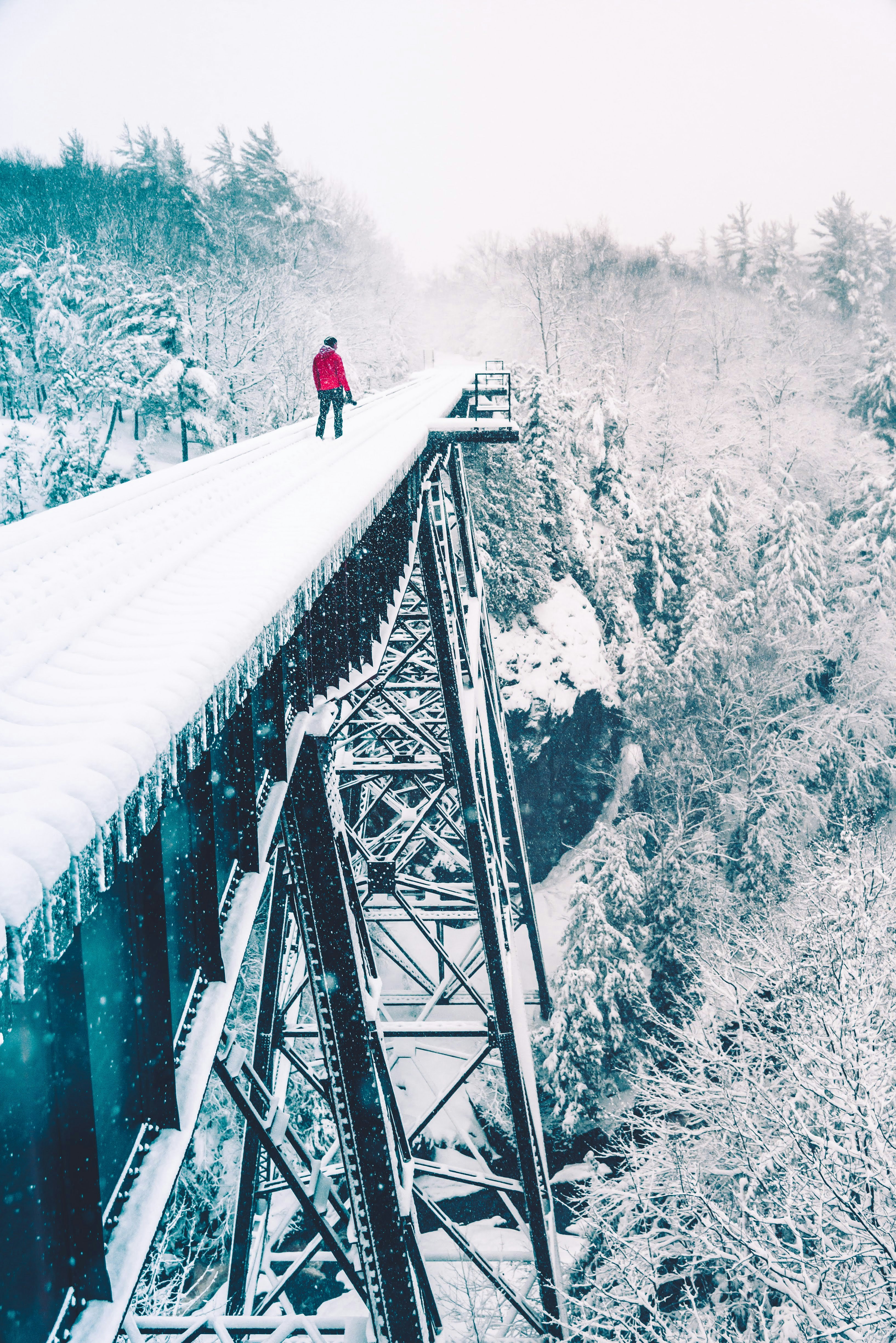 man wearing red jacket walking on the snowy bridge