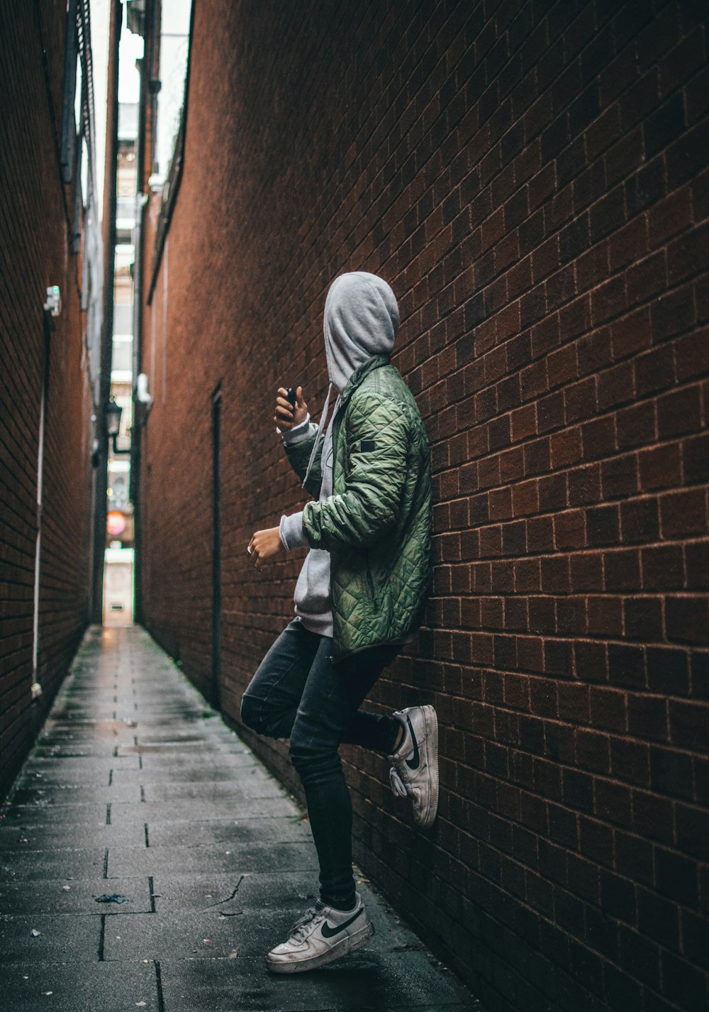 man wearing green hooded jacket standing beside the wall