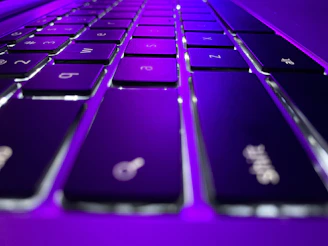 Close-up of hands typing on a sleek keyboard with futuristic purple lighting.