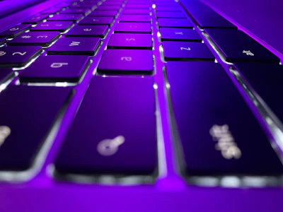 Close-up of hands typing on a sleek keyboard with futuristic purple lighting.