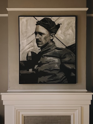 A black and white painting of a person wearing a cap, dressed in what appears to be military attire, is mounted on a wall above a fireplace. The artwork captures a somber expression, with strong shadows accentuating the features.