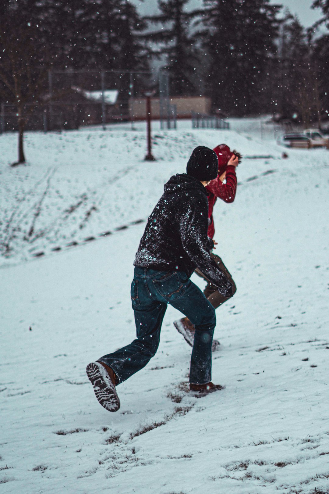 man wearing black hooded jacket walking on the snowy field