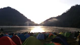 Tents pitched on a serene lakeshore with mist rising in the early morning.