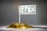 A meticulously arranged pile of shiny gold coins is topped by a rolled paper acting as a pole that holds a one hundred dollar bill. The setup resembles a flag mounted on a mound of wealth.
