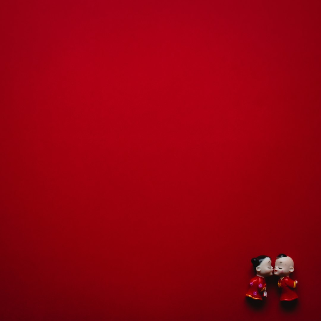 Two figurines, people, embracing in a kiss in the lower far right corner amidst a red background.