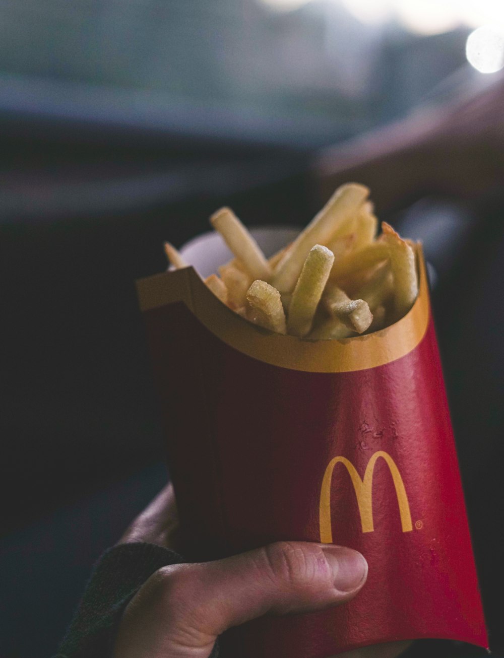 a hand holding a red paper container filled with french fries