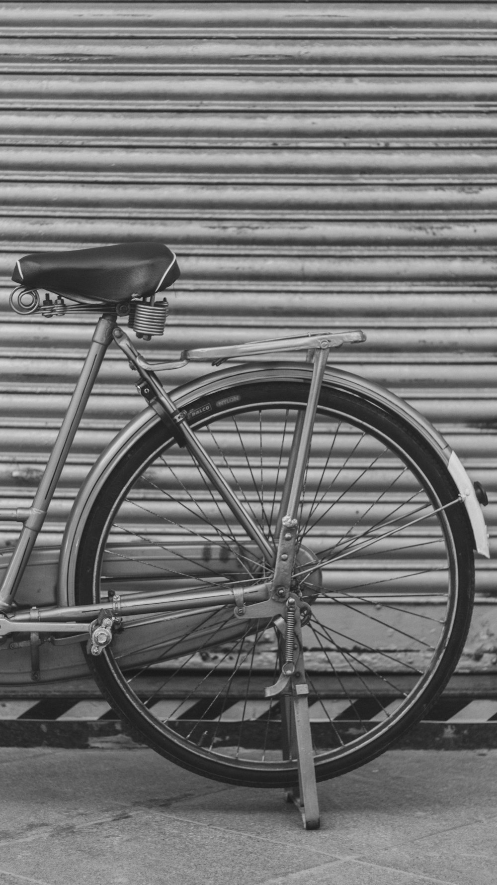 grayscale photo of bicycle parked in front of building with roller shutter