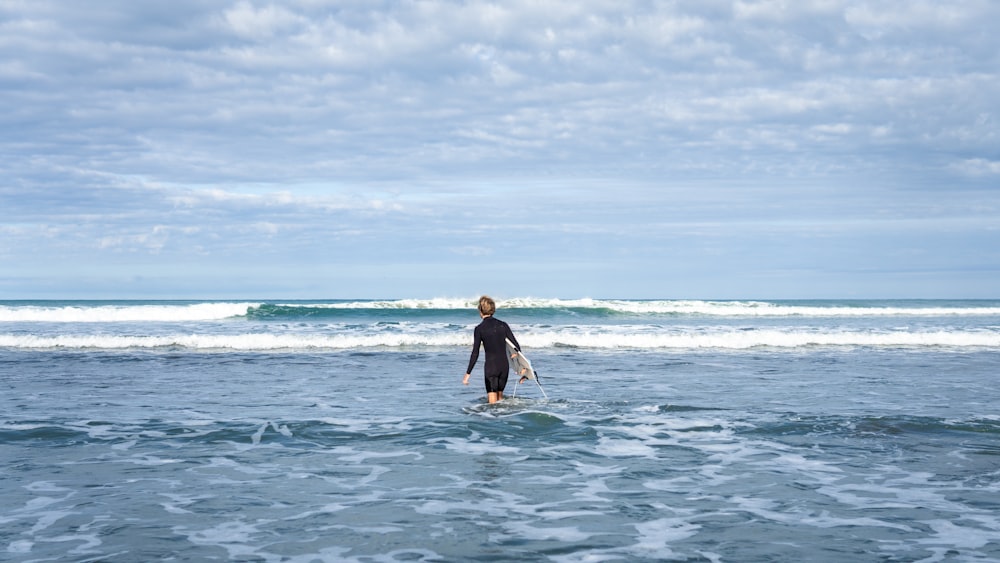 person walking on sea carrying surfboard