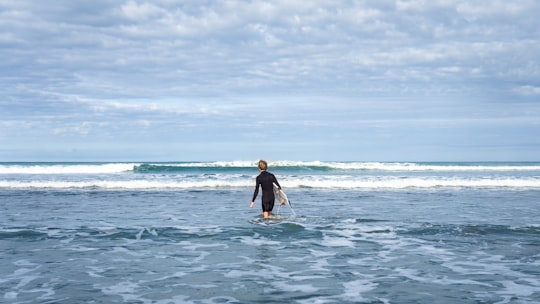 person walking on sea carrying surfboard in Port Waikato New Zealand