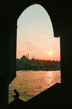 Majestic desert sunset with the silhouette of an Arabian arch framing a figure in regal Muslim attire.