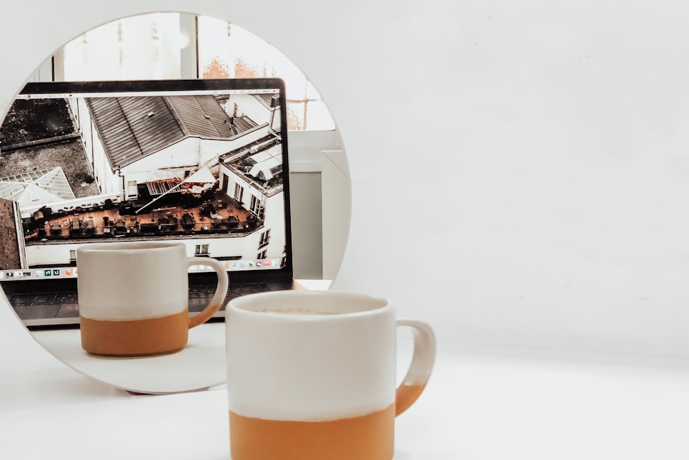 white and brown mug in front of MacBook Pro