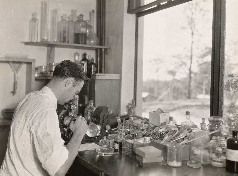 grayscale photography of scientist using microscope in the zoological division 