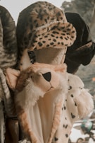 A variety of plush hats designed to resemble animal heads are displayed. The central hat is styled like a cheetah, with spotted fur and a black nose. Other hats feature different animal prints and textures.