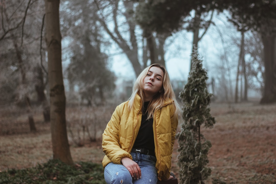 selective focus photography of girl sitting beside green plant during daytime