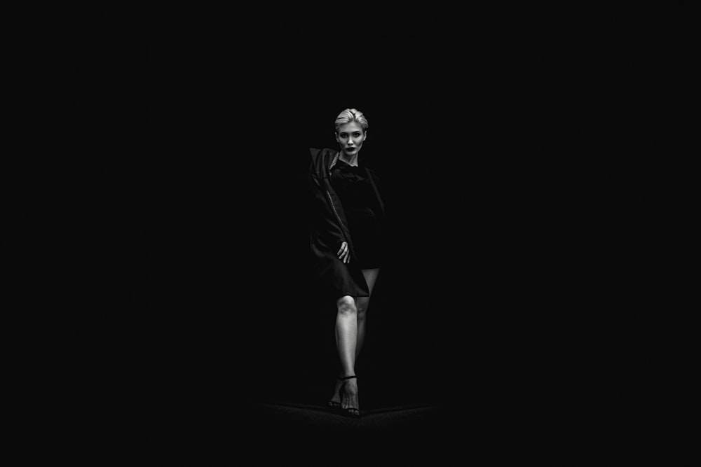 grayscale photo of standing woman near black surface