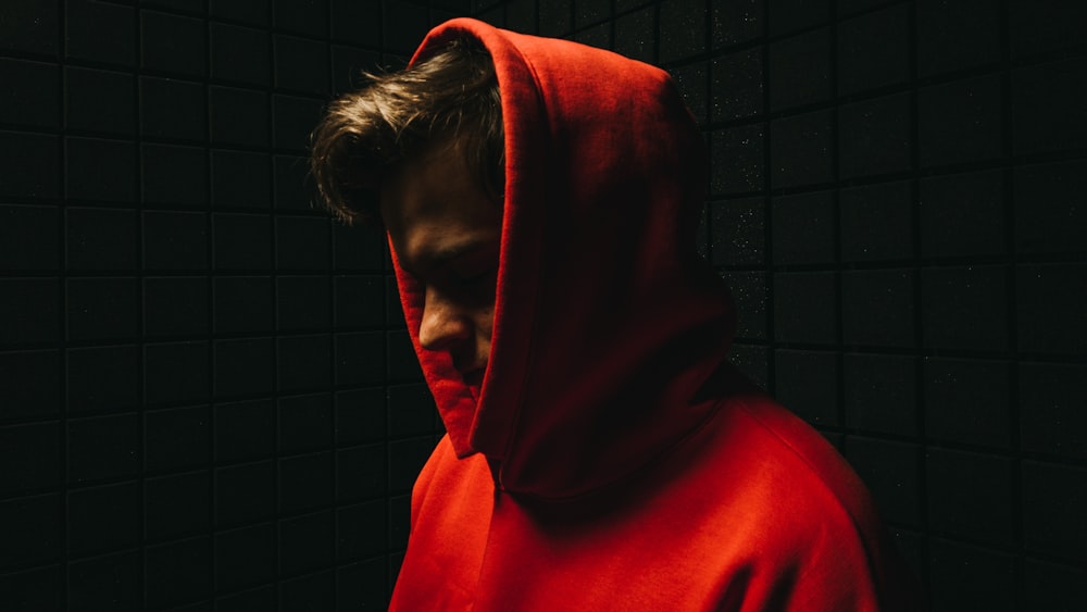 man in red hoodie standing beside wall