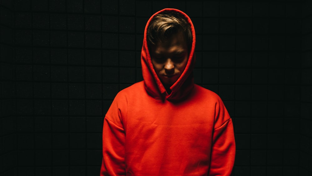 man in red hoodie standing beside wall