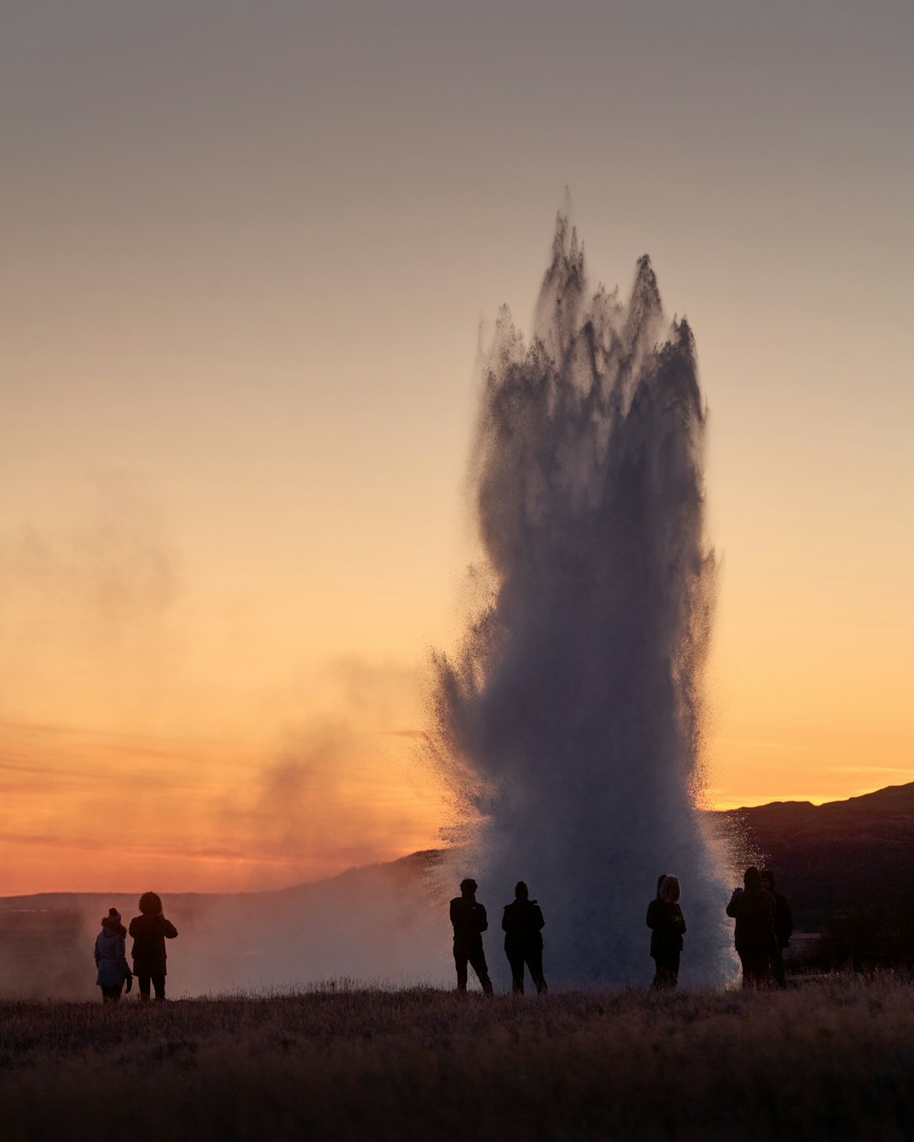 silhouette of people standing beside geyser during sunset