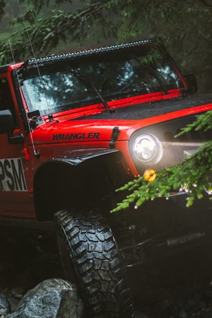 red Jeep Wrangler with rugged car tyres in an off road setting