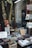 A storefront window displays a collection of old books, magazines, and a sign indicating everything is priced at 1 Euro. A golden harp and various decorations are visible among the items. Outside the window, a person is seen walking past.
