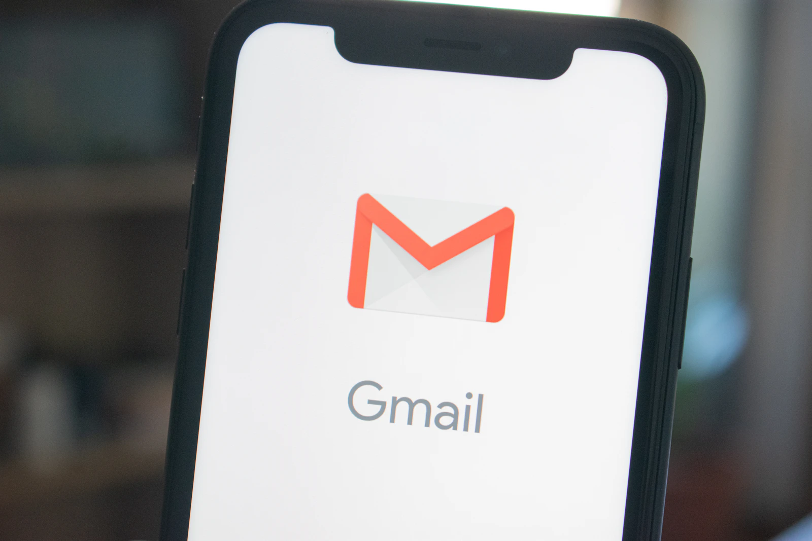 Gmail-logo på smartphone-skærm, dæmpet baggrund i varme toner.