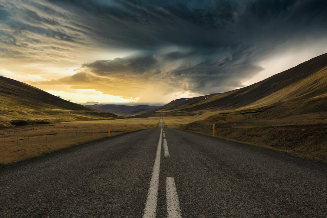 road between brown mountain under cloudy sky