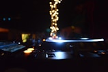 A dimly lit DJ setup with glowing equipment, surrounded by colorful lights and a blurred figure in the background.