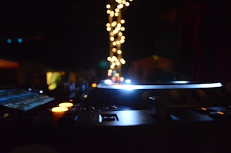 A dimly lit DJ setup with glowing equipment, surrounded by colorful lights and a blurred figure in the background.