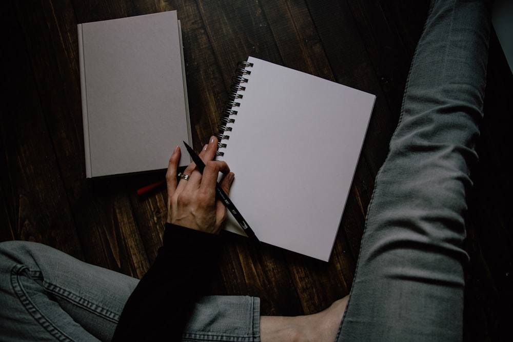 person holding black ballpoint pen and spring notebook